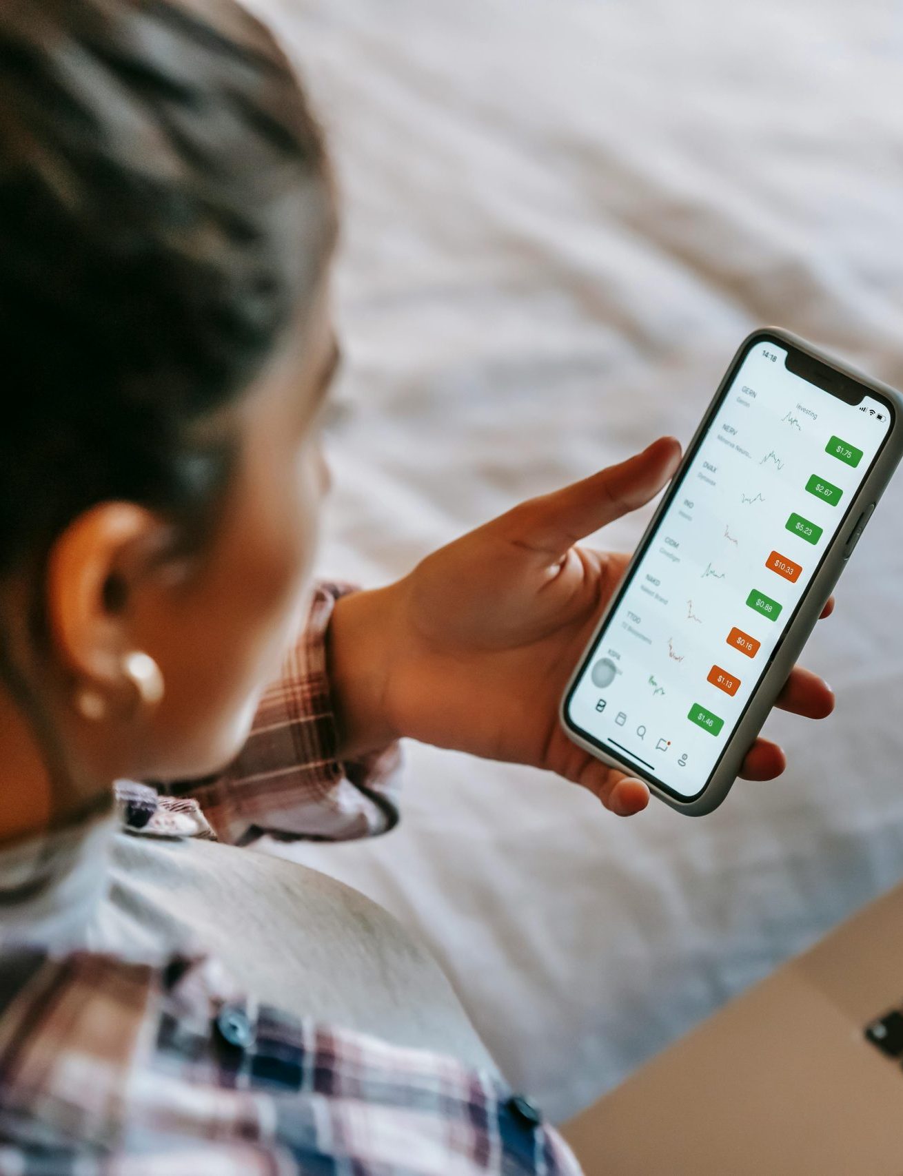 Female analyzing stock market data on her smartphone and laptop indoors. Ideal for finance, technology, and investment themes.